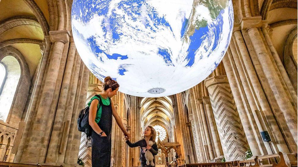 A mother and child pause under the illuminated earth suspended from the nave