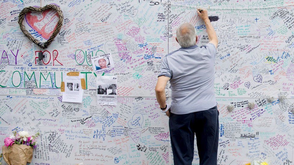 A man writing on a wall in remembrance of those who died at Grenfell Tower