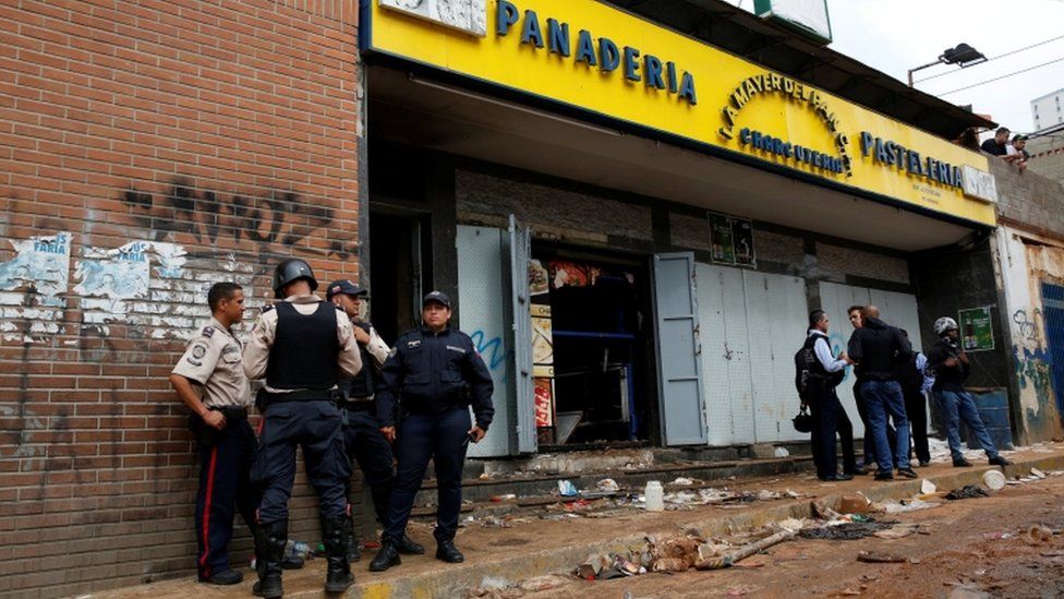 Police officers and criminal investigators look for evidence in front of a bakery, after it was looted in Caracas