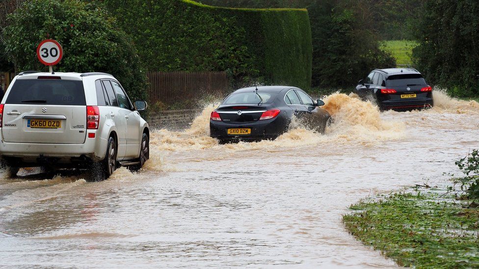 Vehicles are driven through a flooded road in Yapton, West Sussex.