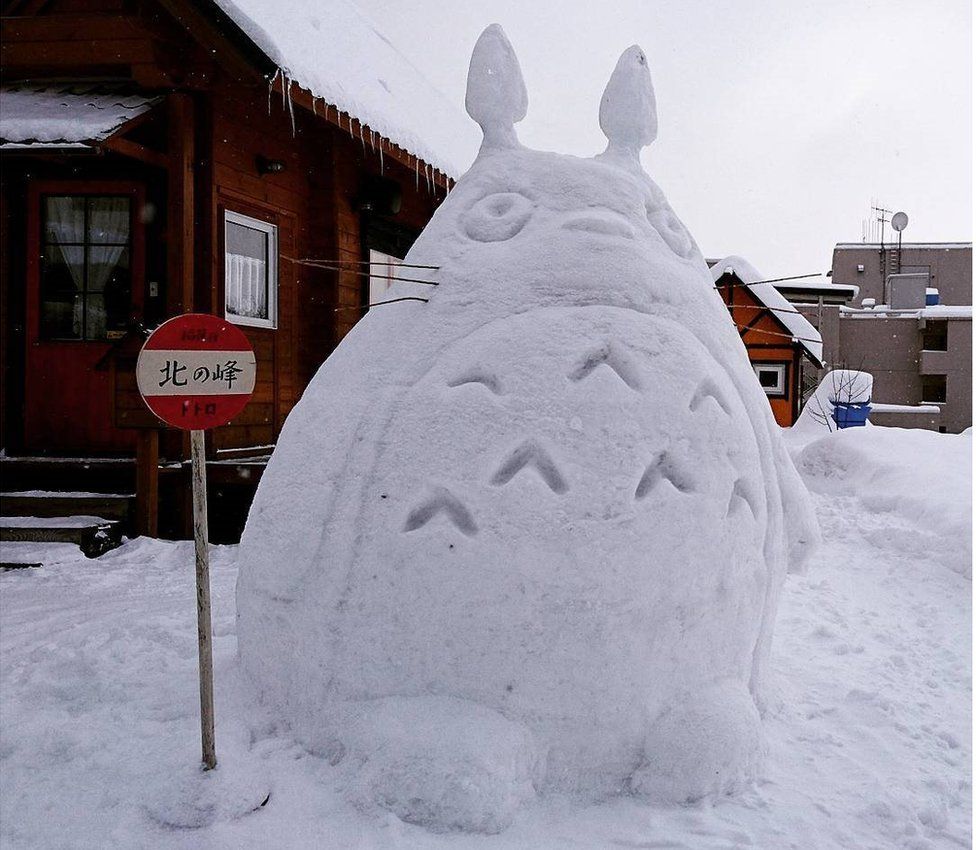 A snow-Totoro standing at a bus stop.