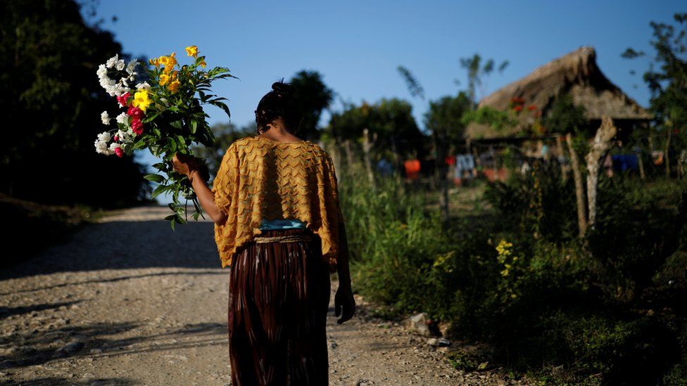 A woman walks with flowers near the home of Jakelin Caal in San Antonio Secortez village, Guatemala