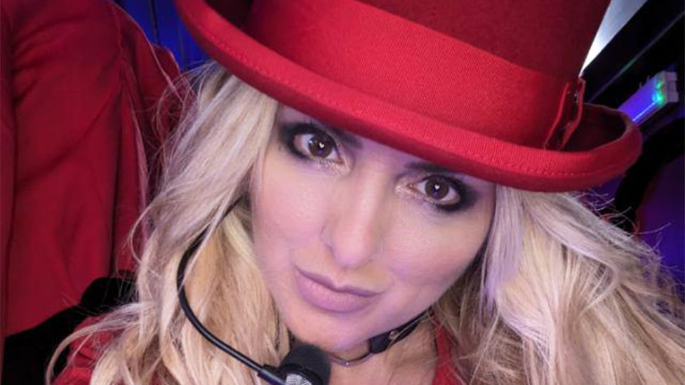 Lucy dressed as a Britney impersonator, looking at the camera. She has blonde hair, a red hat and a black "Britney" mic going from her ear to below her mouth, near her chin.
