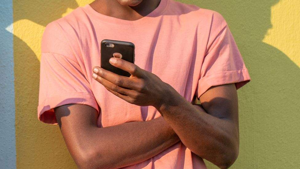 A man with arms crossed looking at a mobile phone