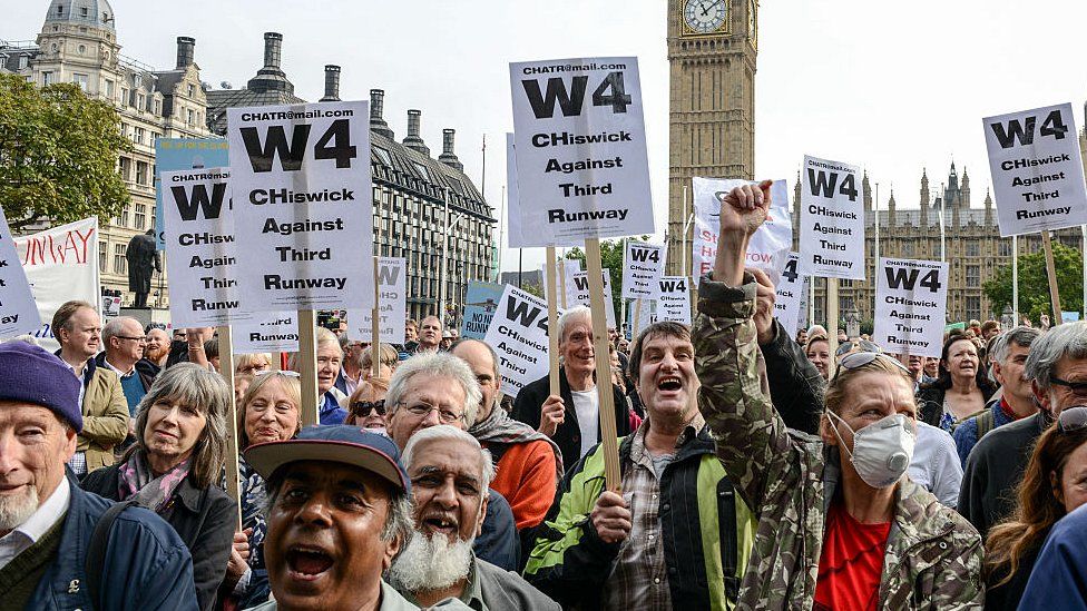 Protesters hold signs during a rally against a third runway at Heathrow airport, in Parliament Square on 10 Oct 2015