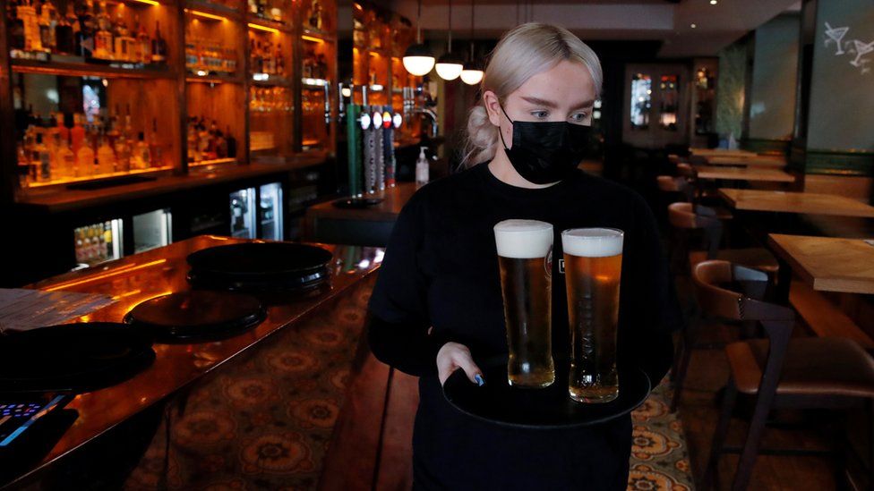 A bar worker serves pints of beer while wearing a mask