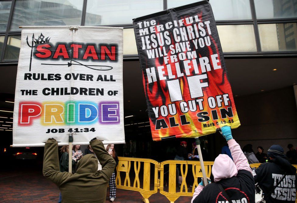 Christian protestors hold up signs outside of the Boston Marriott Copley hotel, as they protest against a convention for Satanists. One reads "Satan rules over all the children of pride". The other says "The merciful Jesus Christ will save you from hellfire if you cut off all sin."