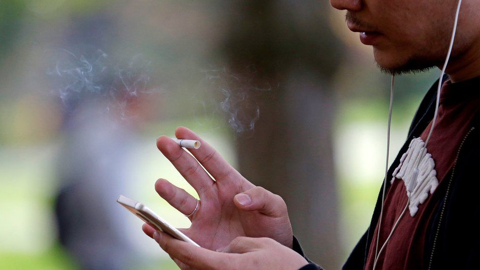 A man smokes while using a smartphone