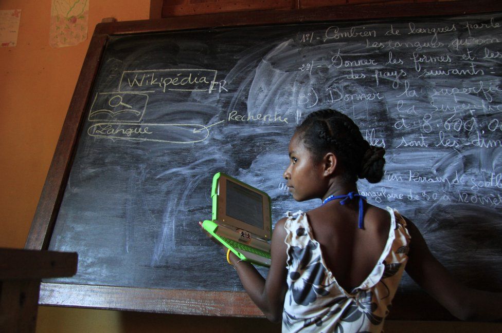 Madagascar, 2012. A girl stands with a laptop next to a black board