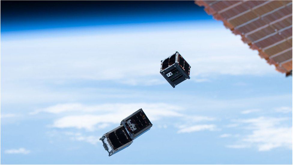 Three CubeSats released from the International Space Station, with Earth behind
