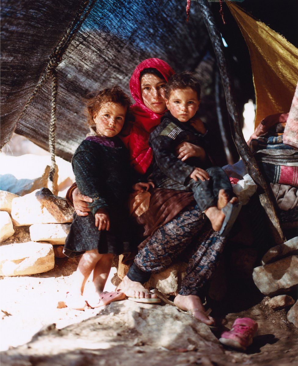 A mother and two children pose for a portrait in a shelter