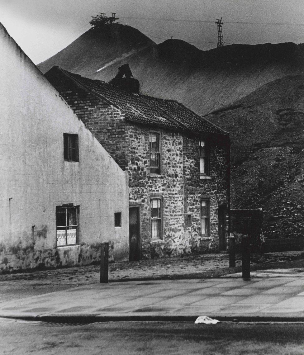 A photograph of cottages with a the hills of a coal mine in the background