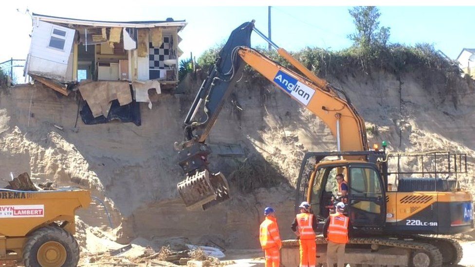 Heavy machinery on the beach clearing debris from collapsed house