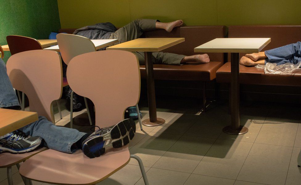 People lying down to sleep on seating in McDonald's