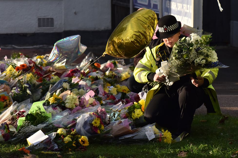 A police officer moves floral tributes for Sir David Amess, which were left near the entrance of the Belfairs Methodist Church, in Leigh-on-Sea, Essex, on 17 October 2021