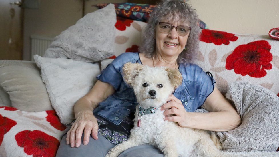 Pip sat on her sofa cuddling a white poodle.