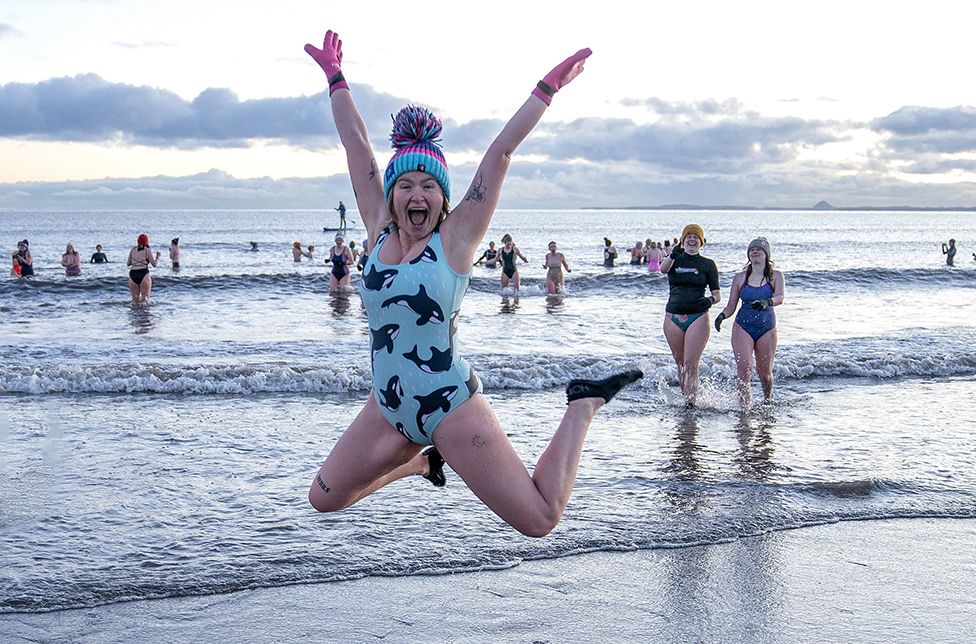 A woman leaps as hundreds of swimmers take a sunrise dip in the Firth of Forth at Portobello Beach, Edinburgh, for International Women’s Day.