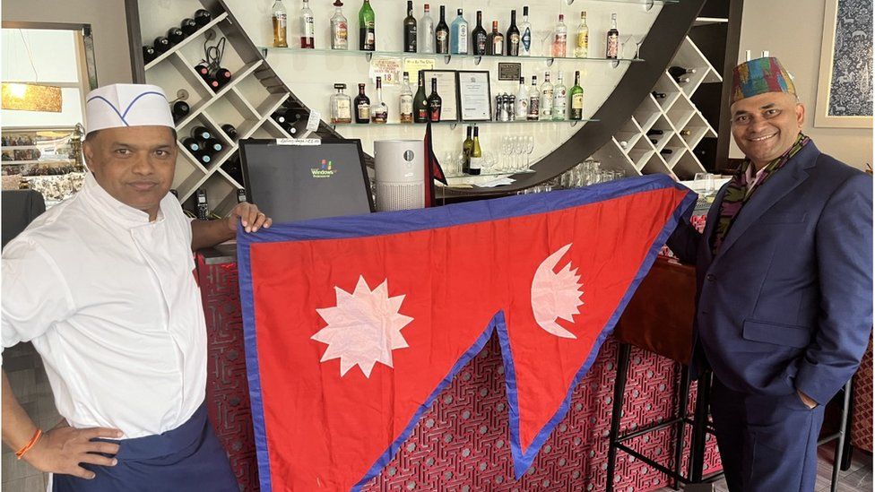Sujan Katuwal holding a Nepal flag at his restaurant