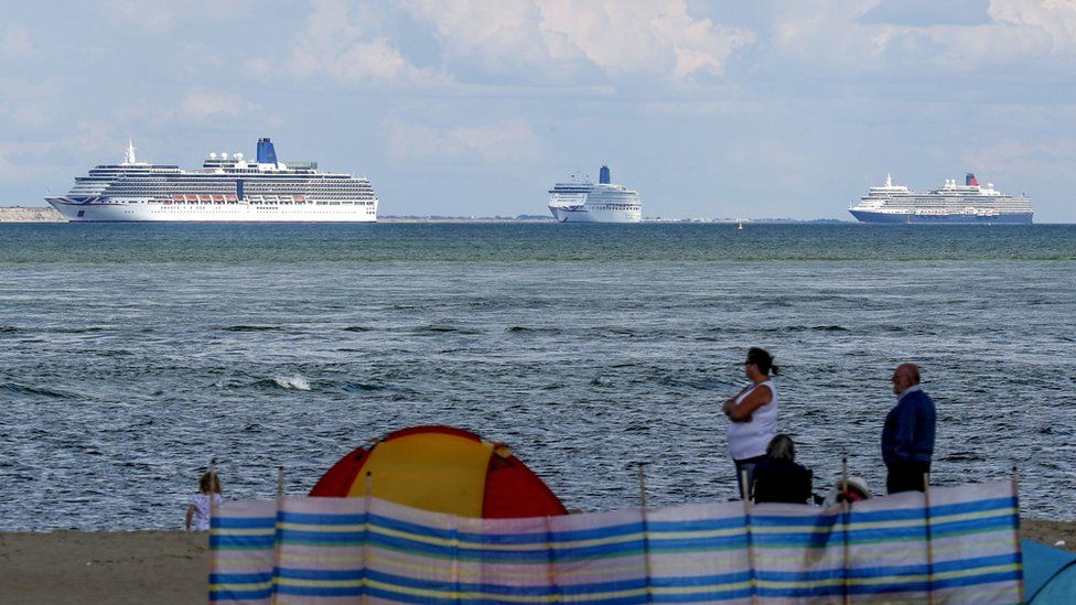 People on the beach at Studland look out at the cruise ships
