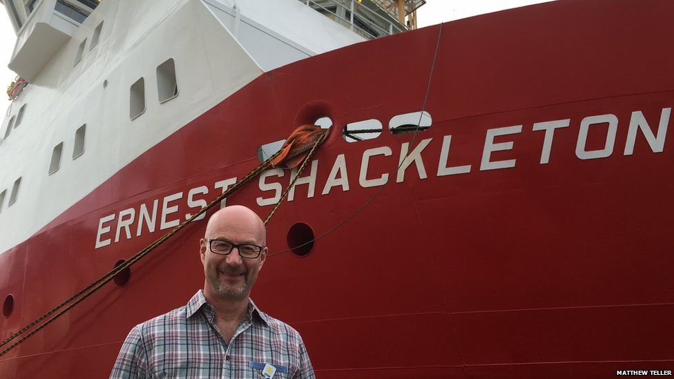 Peter Gibbs in front of the RRS Ernest Shackleton. The ship is red in colour and the name is in big white letters.