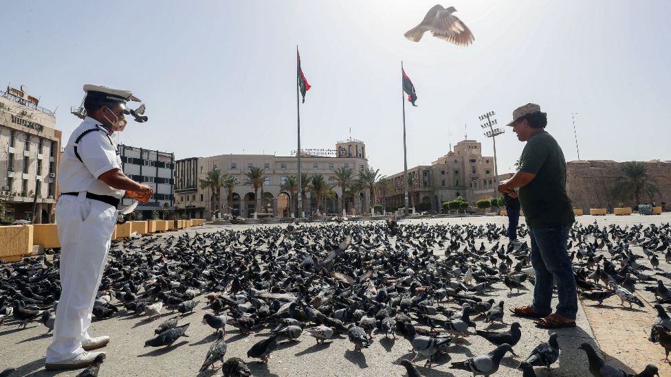 Libyan men feed pigeons in an empty Martyrs Square in downtown Tripoli, Libya - Saturday 7 August 2021