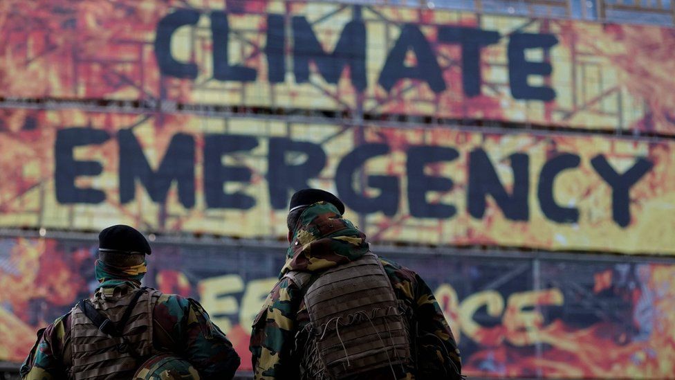 Two soldiers look at a group of activist of the environmental NGO Greenpeace taking part in a protest action after attaching a banner on the frontage of the European Council"s building, in Brussels