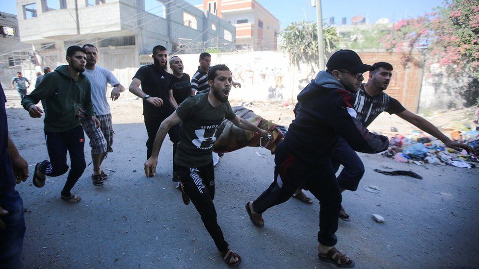 Health team members and civilians carry a wounded man to an ambulance after Israeli fighter jets conducted airstrikes towards a building in Al-Bureyc refugee camp of Gaza Strip, Gaza on May 13, 2021