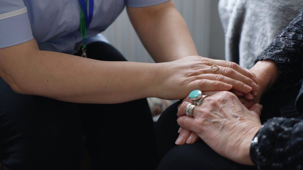 A social carer holding hands with an elderly person