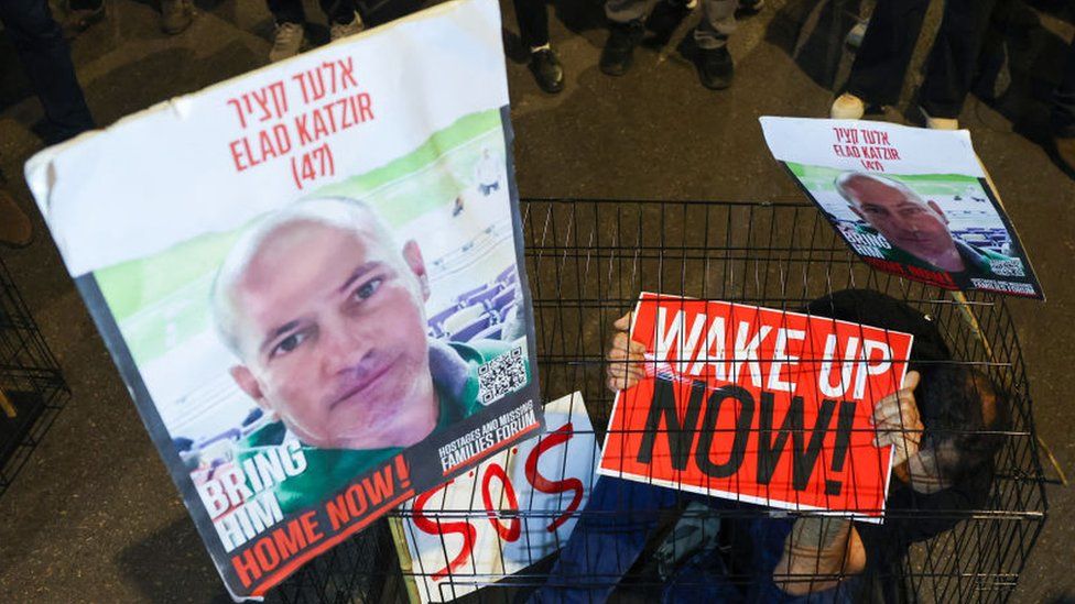 A man sits in a cage with portraits of hostage Elad Katzir during a demonstration in Tel Aviv in March
