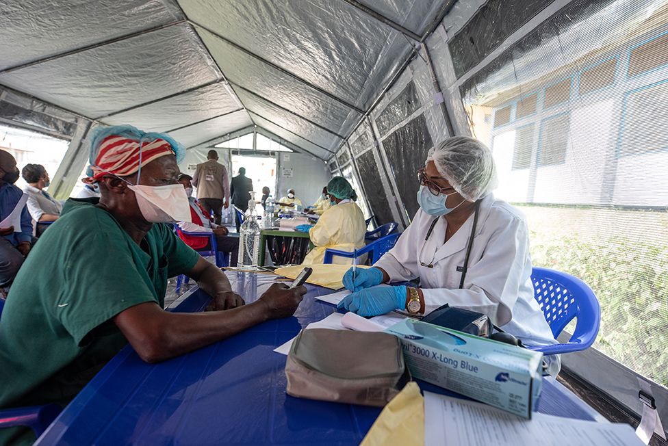 A health worker wearing a mask gives his details to a nurse in the vaccine tent