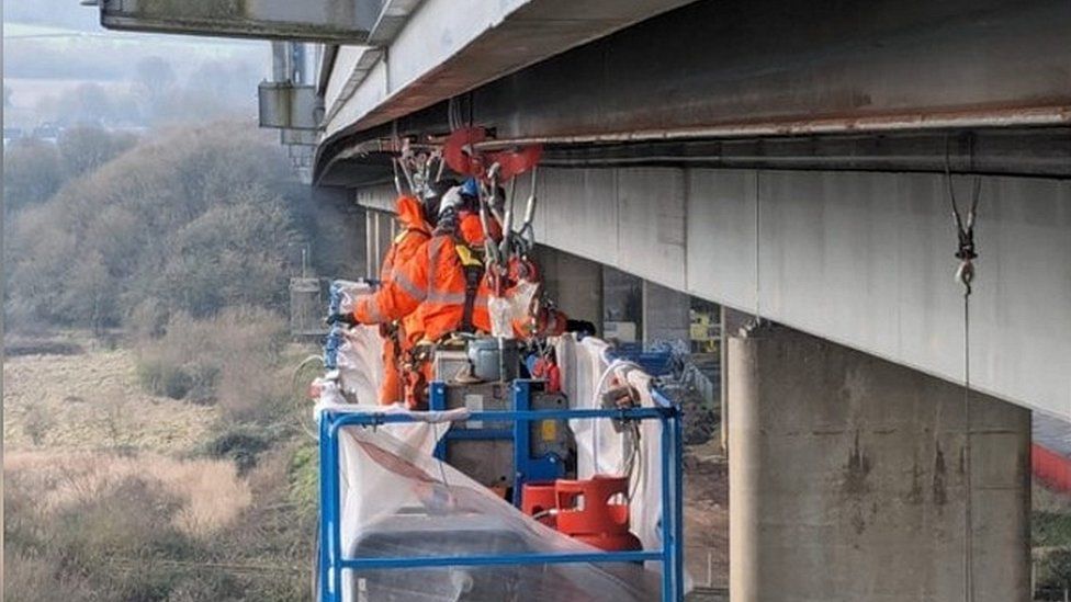 Inspection work takes place on a runway beam under the bridge parapets