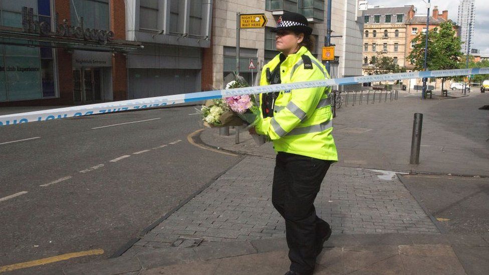 A police woman carries floral tributes to the victims of the attack on Shudehill, May 23, 2017 in Manchester