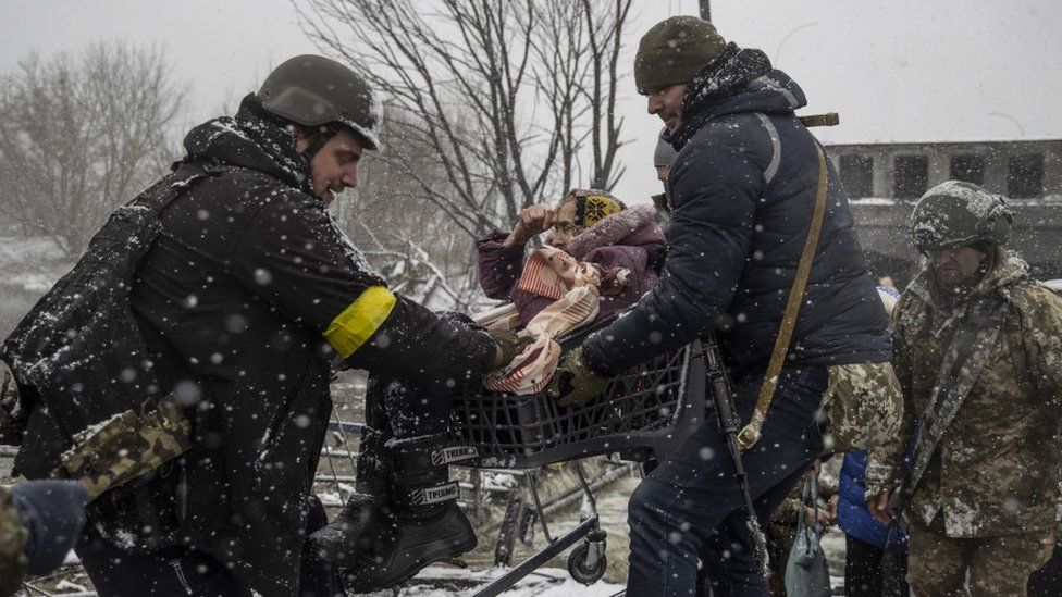 Officers evacuate an elderly woman as civilians continue to flee from Irpin due to ongoing Russian attacks as snow falls in Irpin, Ukraine on March 08, 2022