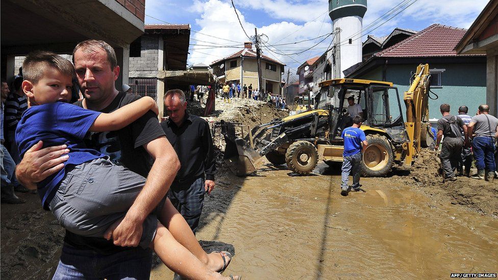 A man carries a child along a flooded street in the village of Sipkovica on 4 August 2015