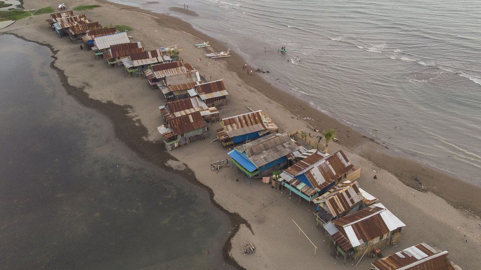 Overhead view of shacks on a sandy spit of land with water on both sides