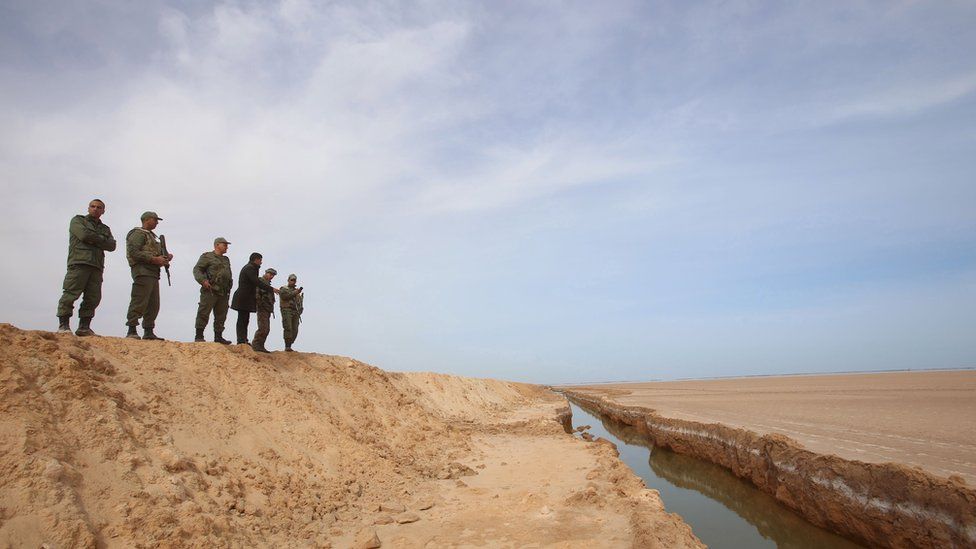 Soldiers overlook a trench, that forms part of a barrier along the frontier with Libya, in Sabkeht Alyun
