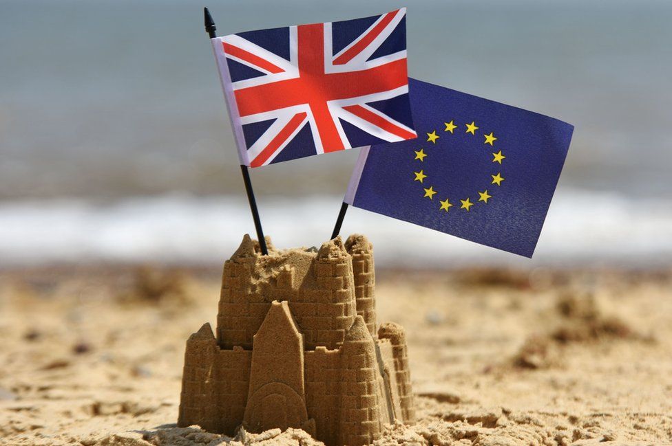 A sandcastle, with the Union and European Union flags flying from its top, on a beach