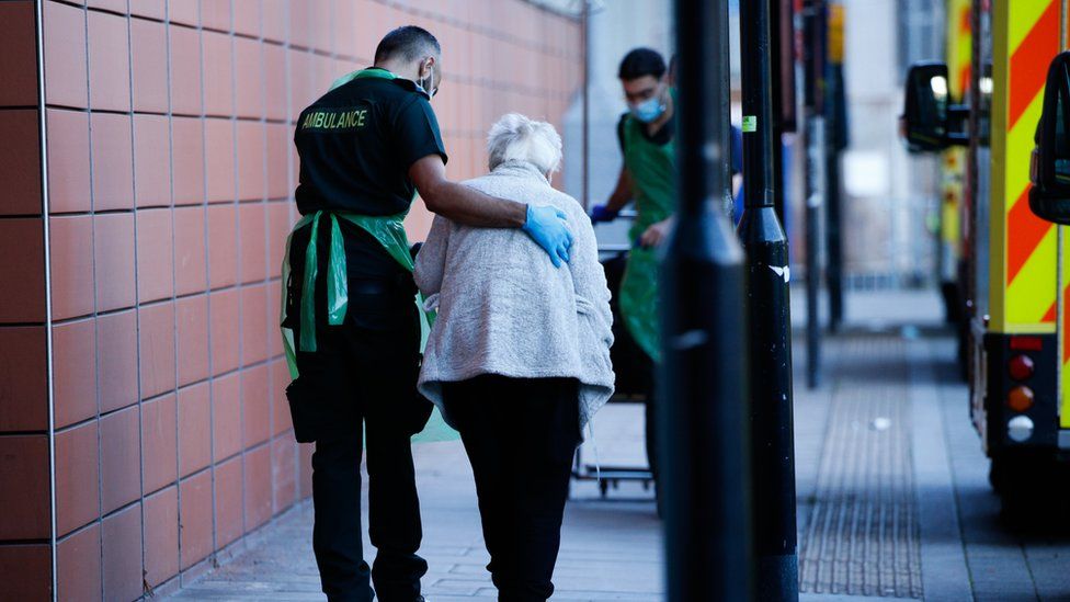 A healthcare worker leading an elderly woman