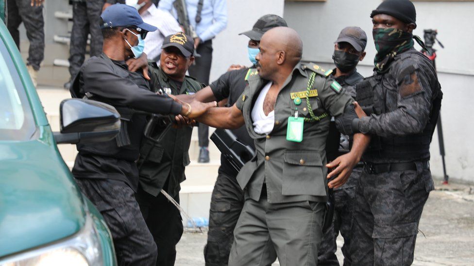 Four men in police camouflage dragging a man in a green uniform