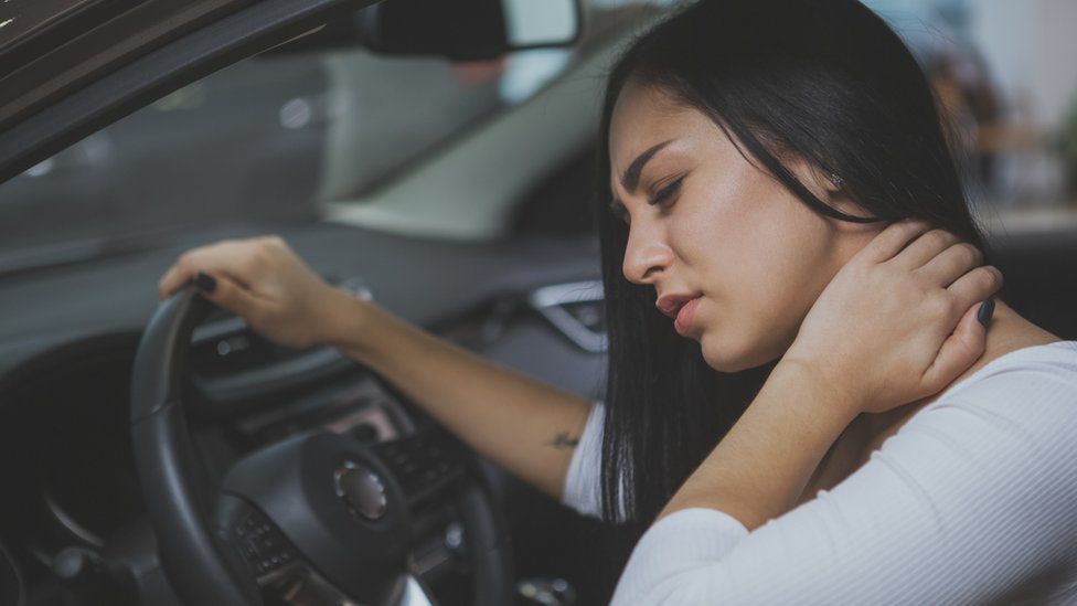 Женщина потирает шею после травмы шеи в машине