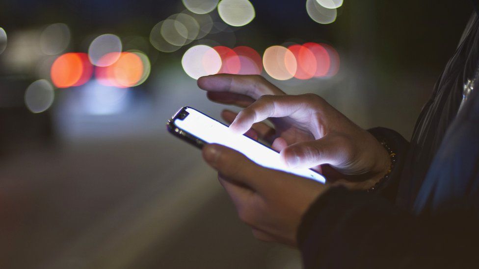Stock image of a man looking at a smartphone screen at night