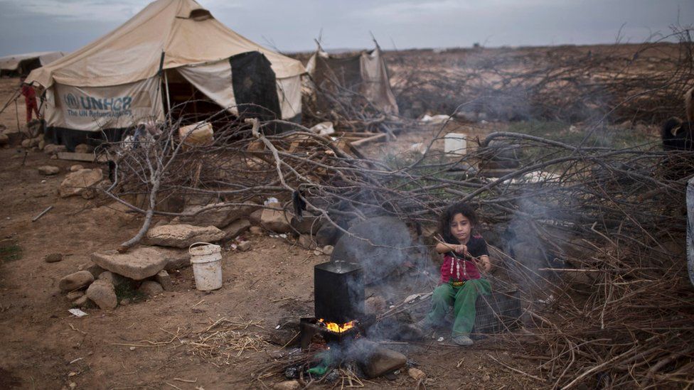 Syrian refugee Aysha Elwan, 5, helps her mother to break wood for a fire outside her family's tent at an informal settlement on the Syria-Jordan border at Mafraq