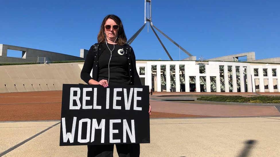 A protester stands outside Parliament House in Canberra holding a sign which reads 'Believe Women'