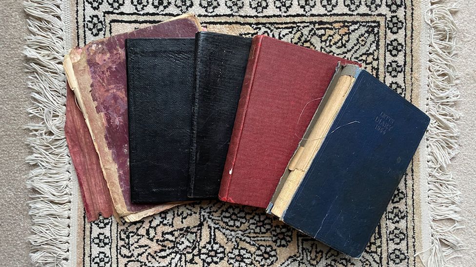 Five battered hardback diaries spread out on a rug