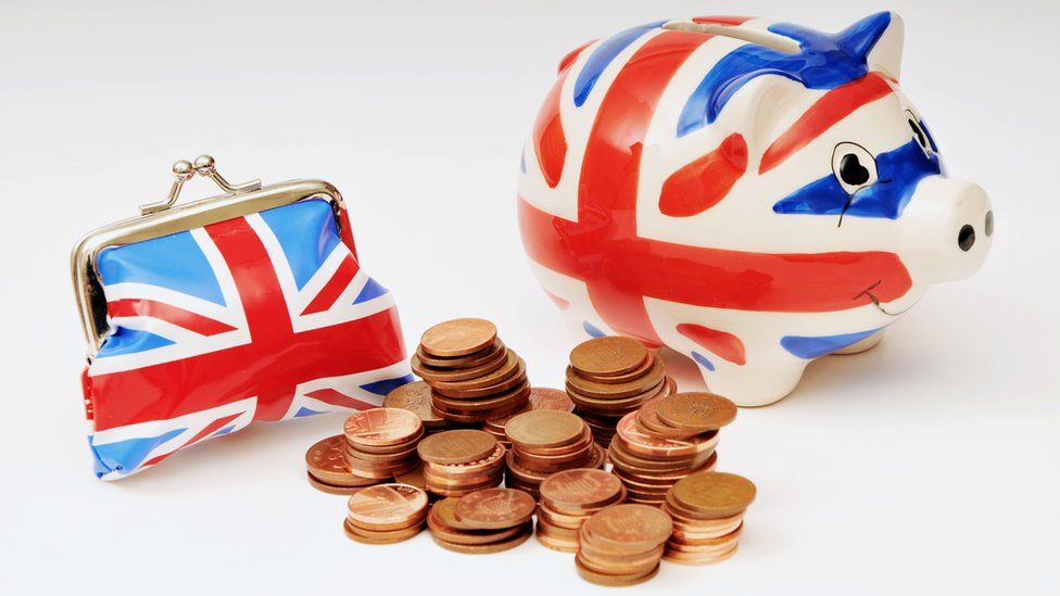 A small purse and piggy bank in Union Jack colours with a pile of UK one and two pence coins
