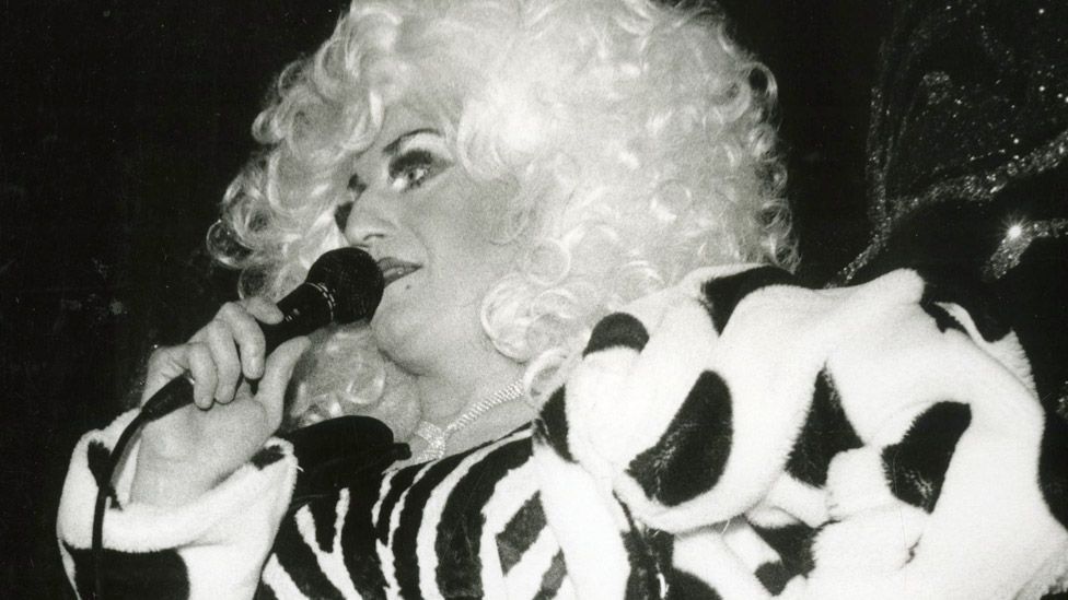 Black and white photograph of Lily Savage speaking into a microphone at the Lighthouse Benefit at the Royal Vauxhall Tavern (26 January 1990)