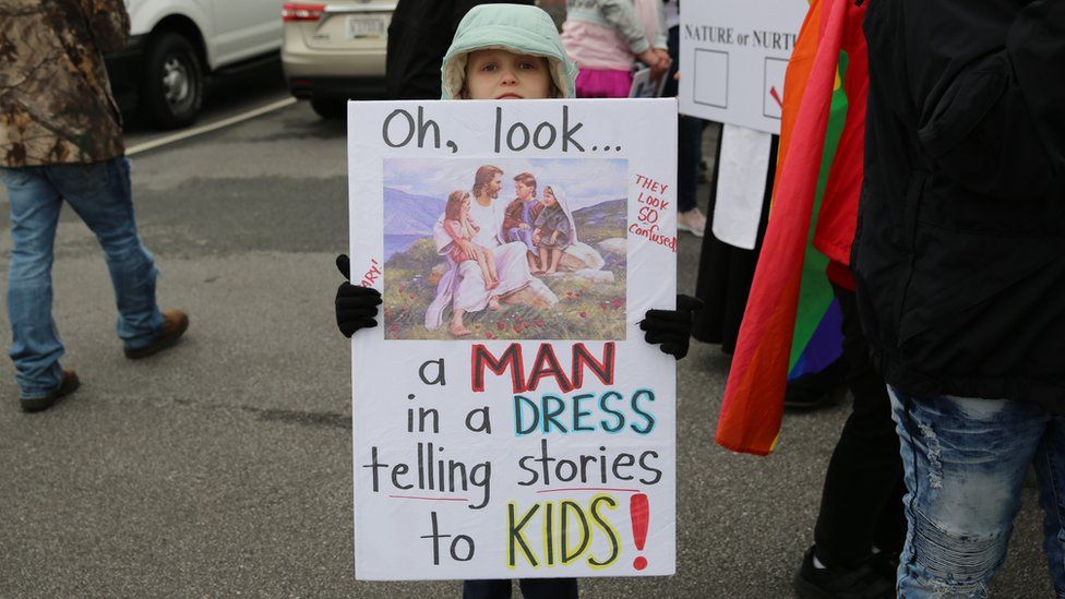 A child holding a sign in support of the drag queen story hour event