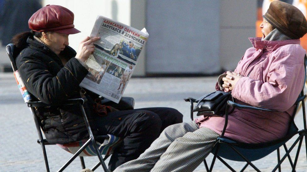 A woman reads a newspaper in Kazakhstan while another looks on.