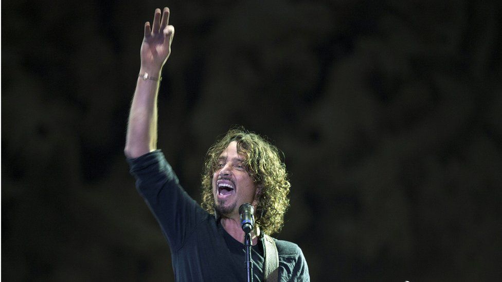 Chris Cornell on stage, raising his hand high as he plays guitar