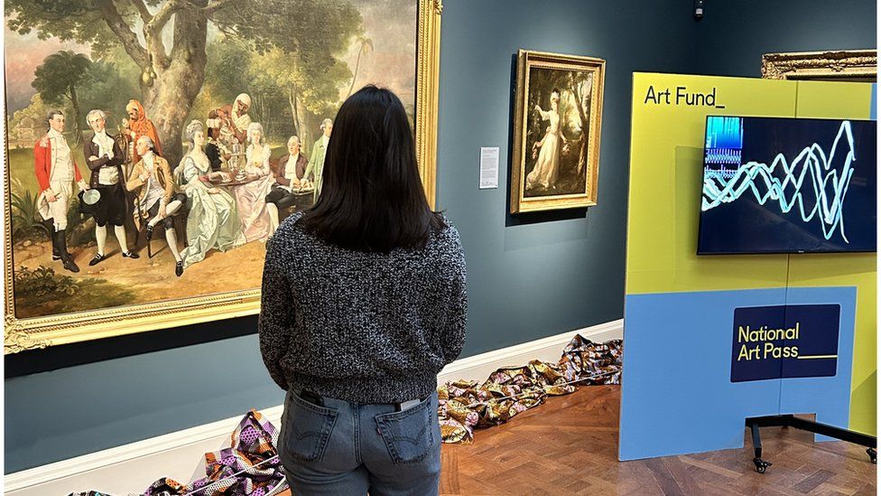 Back of a woman who is standing looking at a painting on a wall at a gallery